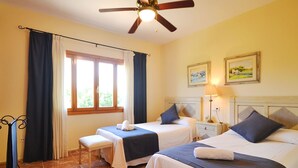 Une chambre d’hôtel avec deux lits, un ventilateur de plafond, une fenêtre avec des rideaux, une table de chevet avec une lampe et un tableau au mur.