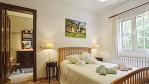 Un dormitorio con una cama de madera, dos mesitas de noche con lámparas, un cuadro en la pared y una ventana con cortinas.