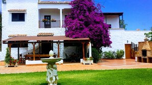 Ein weißes Gebäude mit einer überdachten Terrasse, einer Statue und einem großen Bougainvillea-Baum in Lila.