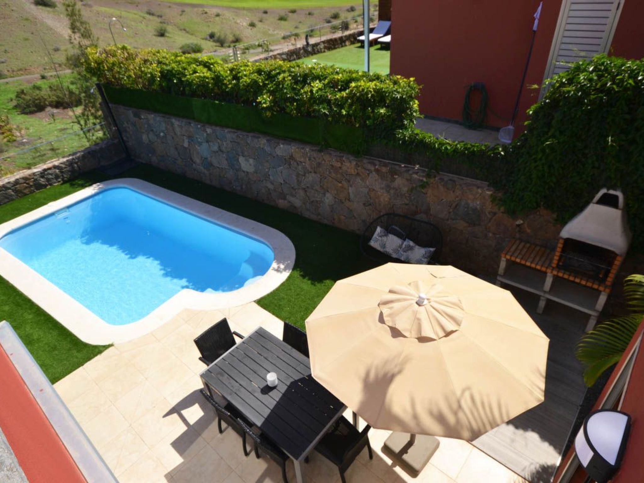 Un patio trasero con piscina, mesa de jardín con sillas y una parrilla.