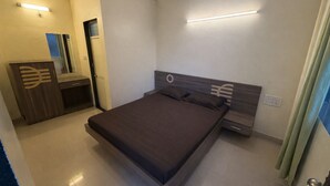 A bedroom with a bed, bedside tables, a wardrobe, and a mirror. - Hotel rosewood plaza - Mahabaleshwar  (Mahabaleshwar)