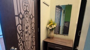 A hallway with a decorative door, a small console table with a vase of flowers, a mirror, and a patterned rug. - Hotel rosewood plaza - Mahabaleshwar (Mahabaleshwar)