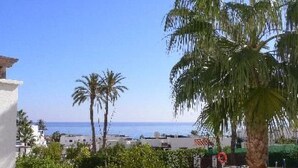 Poolbereich mit Palmen und Blick auf das Meer.