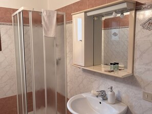 Un bany amb un plat de dutxa de vidre, un rentapeus, un mirall i una tovallola penjada a la porta de la dutxa.