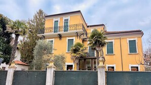 Ein zweistöckiges Gebäude mit gelber Fassade, grünen Fensterläden und einem Balkon mit schmiedeeisernen Geländern.