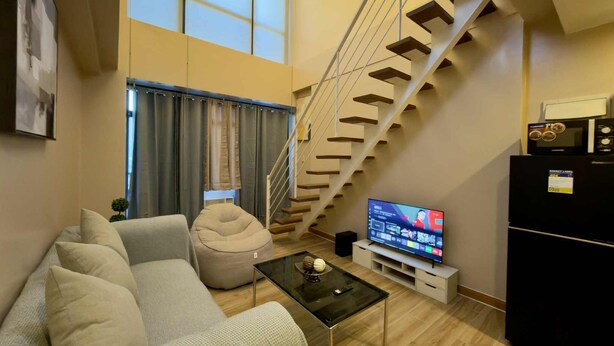 A modern living room with a sofa, a glass coffee table, a flat-screen TV, a black refrigerator, and a staircase. - Makati City Poblacion 1 bedroom  (Makati)