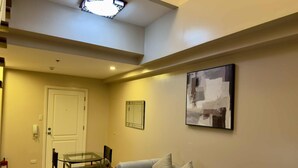 A living room with a sofa, a glass coffee table, a dining table with chairs, a white door, and a ceiling light fixture. - Makati City Poblacion 1 bedroom  (Makati)