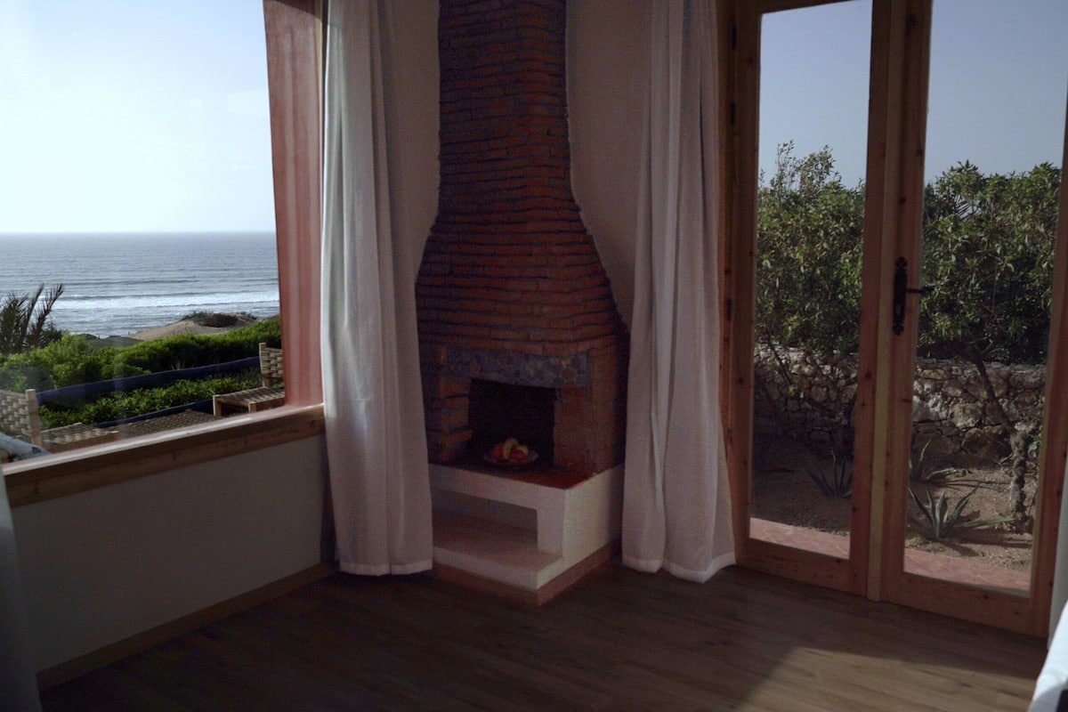 Una habitación con chimenea, vistas al océano y un balcón con pared de piedra.