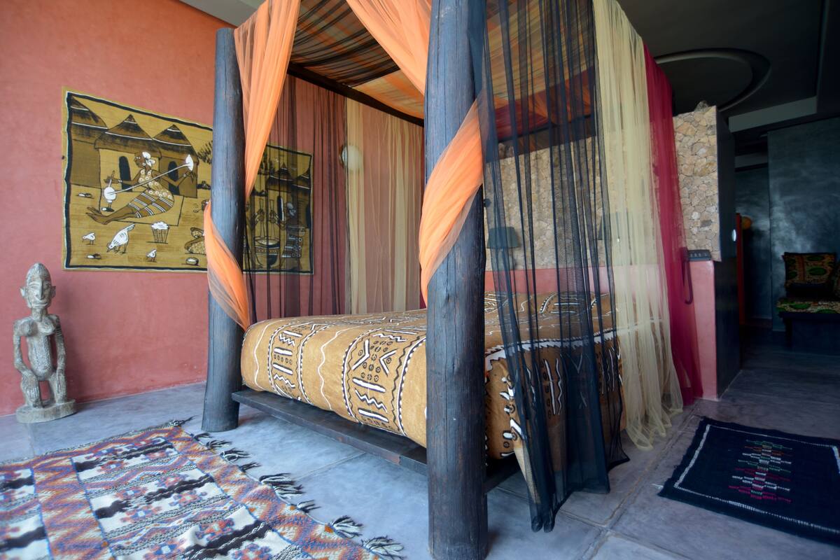 Una cama con dosel con una colcha estampada, una pintura decorativa en la pared y una estatua de piedra.
