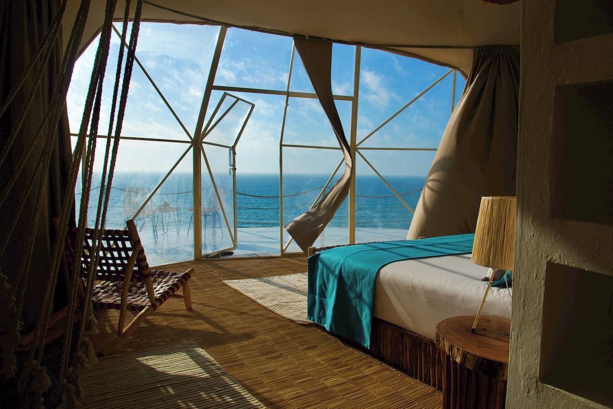Una habitación con un ventanal grande, una cama, una silla y una mesita.