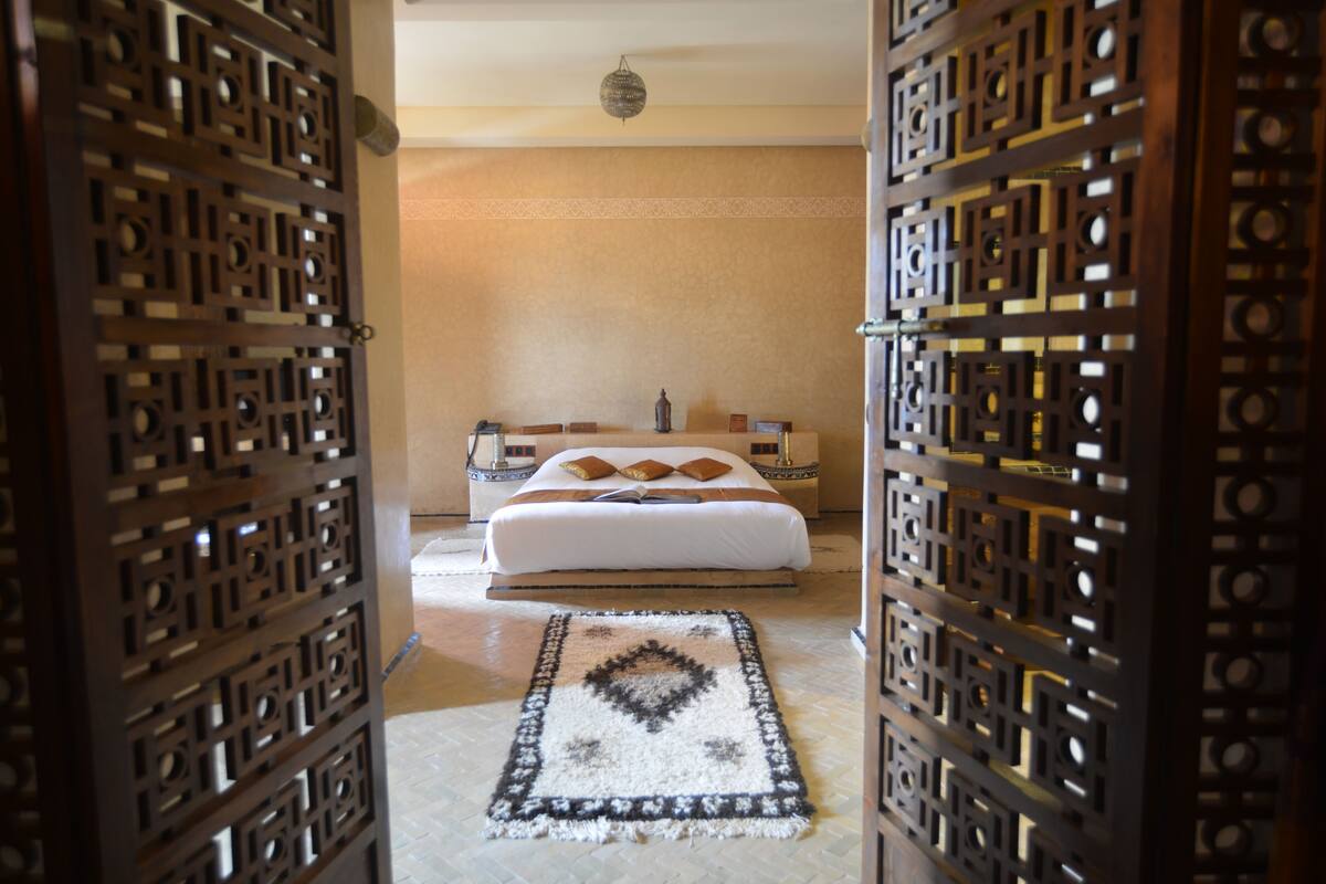 Un dormitorio con cama, mesitas de noche, una pared decorativa y una alfombra estampada.