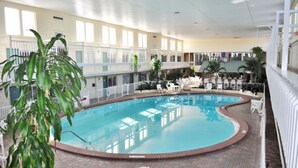 Une piscine intérieure avec un sol en briques, entourée de chaises longues blanches et de plantes en pot.