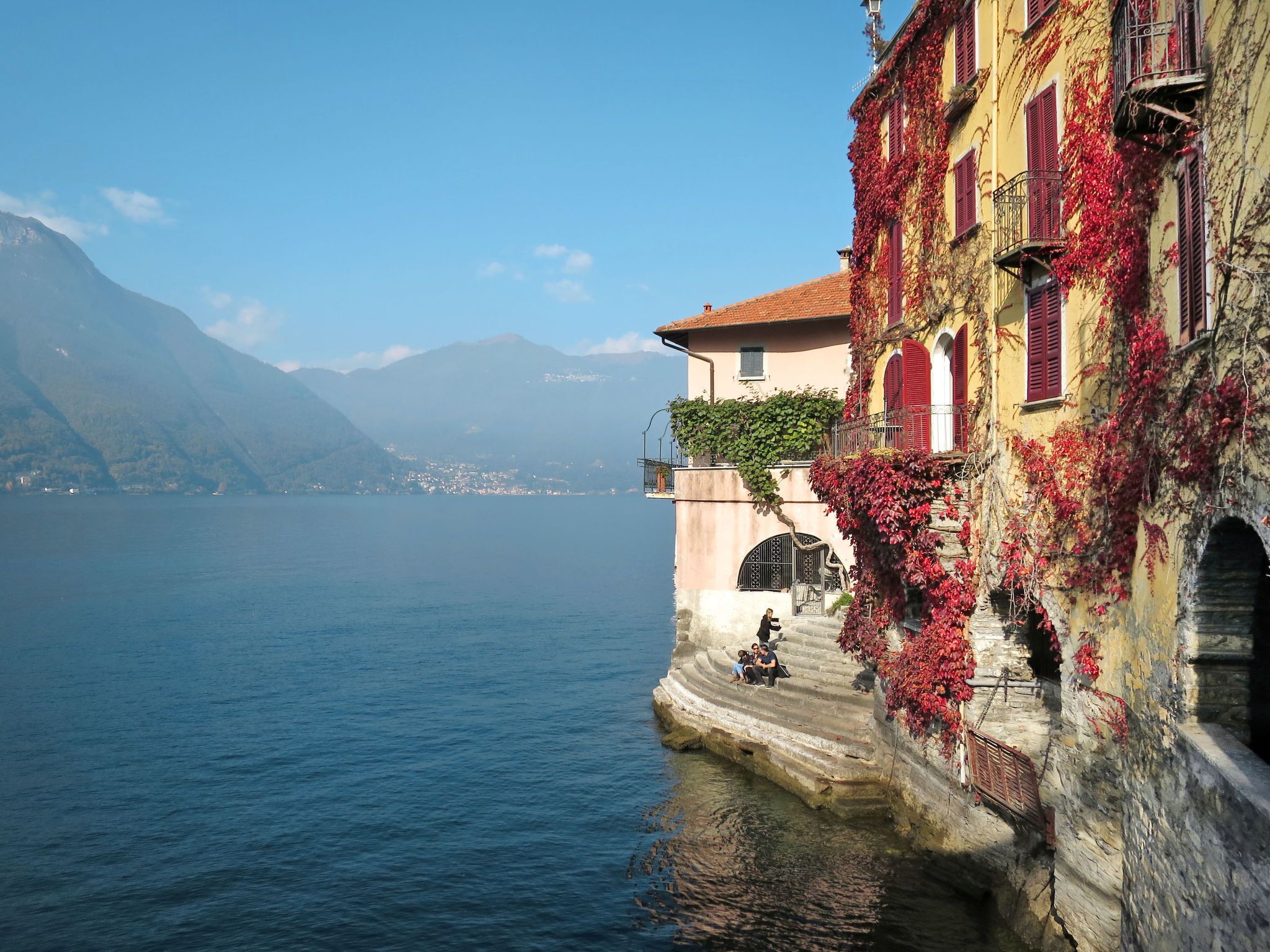 A waterfront building with red shutters and a stone staircase leading down to the water.