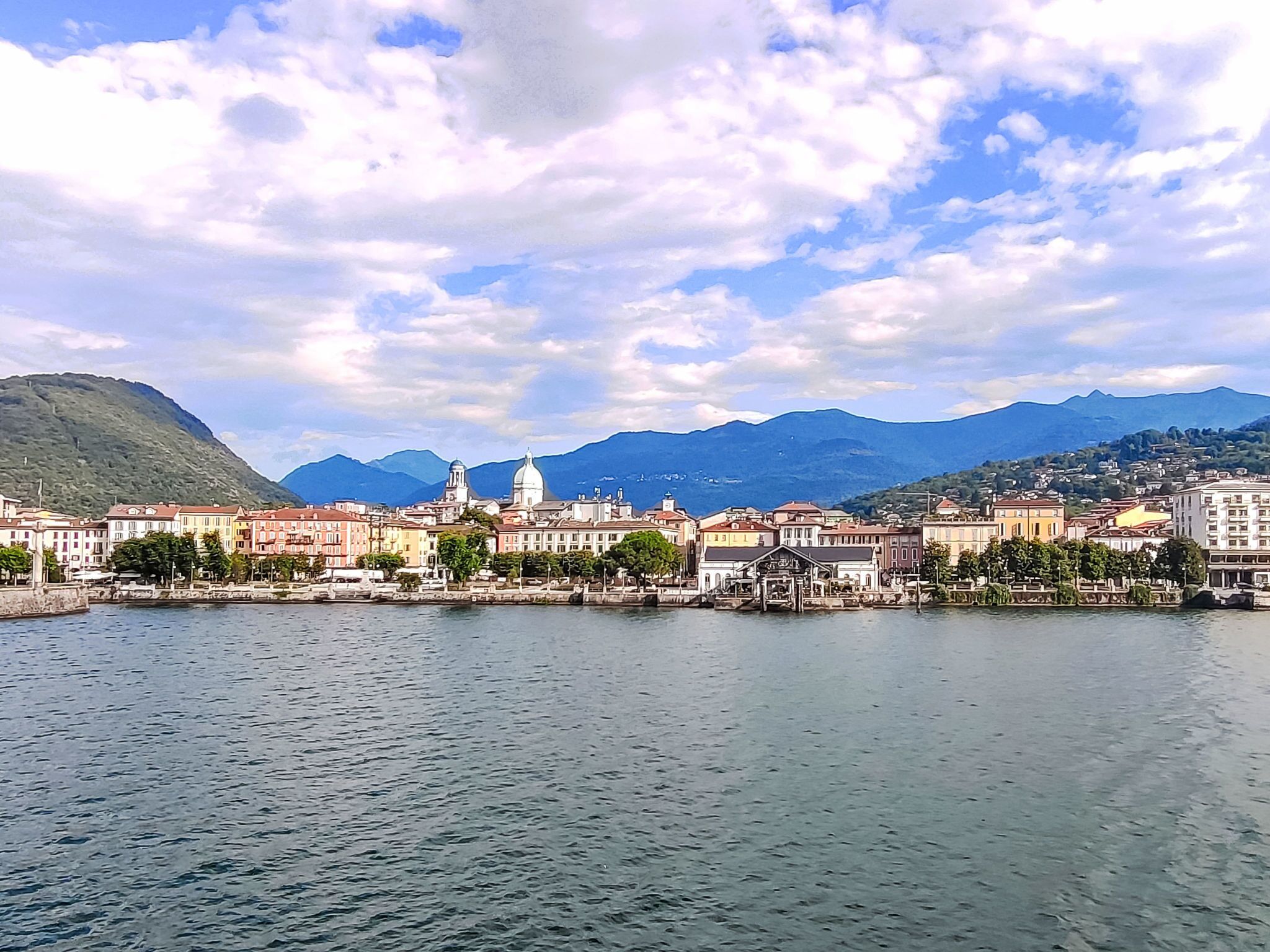A waterfront cityscape with historic buildings, a prominent dome, and mountains in the background.