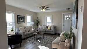 A living room with a gray sofa, a black armchair, a coffee table, and a ceiling fan. - Wine Trail and Sunset Vibes in this Welcoming 3-bedroom home in Cayuga! (Cayuga)