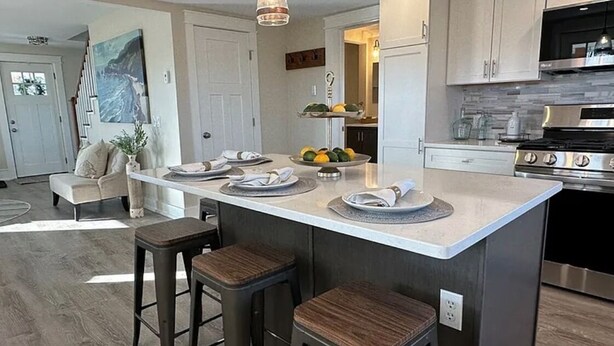 A modern kitchen with a large island, bar stools, pendant lighting, and stainless steel appliances. - Wine Trail and Sunset Vibes in this Welcoming 3-bedroom home in Cayuga! (Cayuga)