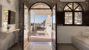 Ένας ευρύχωρος διάδρομος με πέτρινους τοίχους, με καθαρή θέα προς το εξωτερικό, ένα παγκάκι και ένα μικρό τραπέζι με μια γλάστρα.