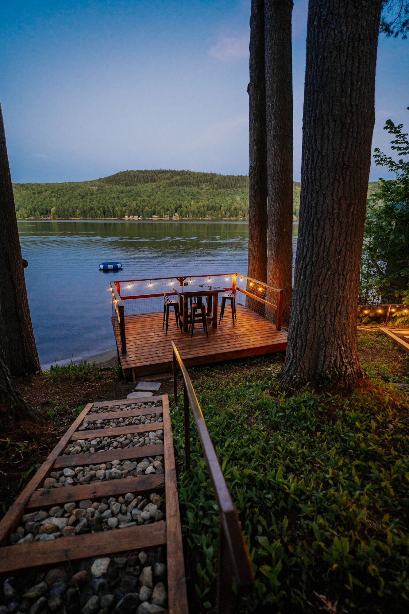 A wooden deck with a table and chairs, overlooking a lake.
