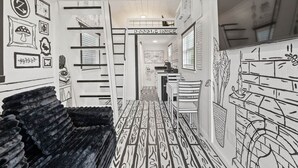 A room with a bunk bed, a desk, and a chair. There is a sign that says "Doodle House" and a wall with drawings. - The Doodle House | Lake Front Tiny Home (Bastrop County)