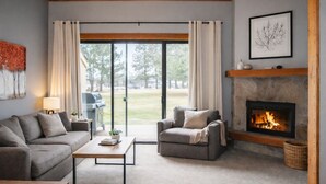 A living room with a stone fireplace, two sofas, a coffee table, and a large sliding glass door leading to a backyard. - Black Butte Ranch Lodge Condo 031 (Black Butte Ranch)