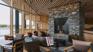 A modern lounge with stone walls, wooden ceiling, and large windows overlooking a body of water. - Black Butte Ranch Lodge Room 030 (Black Butte Ranch)