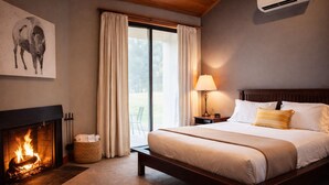A bedroom with a fireplace, a bed with white bedding, a nightstand with a lamp, and a painting of a bull on the wall. - Black Butte Ranch Lodge Room 030 (Black Butte Ranch)