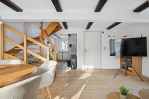 A modern living room with a wooden staircase, a flat-screen TV on a stand, and a dining area with a round table and chairs.