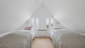 Et soveværelse med to senge, hvide vægge, et skråt loft og et vindue.