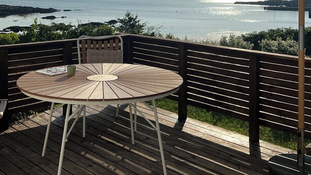 Une terrasse en bois avec une table ronde et des chaises, un parasol et une vue sur la mer.