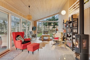 A modern living room with a large window, a red armchair, a fireplace, and a bookshelf. - Cosy private cottage 800 m from the beach (Løkken)