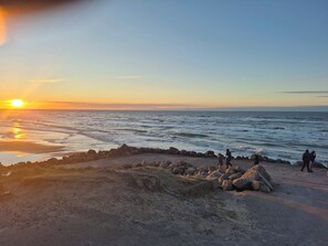 A beach with a rocky shoreline, waves, and the sun setting over the horizon. - Cosy private cottage 800 m from the beach (Løkken)