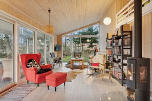 A modern living room with a large window, a red armchair, a fireplace, and a bookshelf. - Cosy private cottage 800 m from the beach (Løkken)