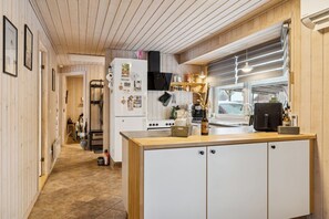 A kitchen with wooden cabinets, a refrigerator, and a window with blinds. - Cosy holiday home near Legoland (Hovborg)