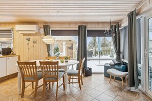 A modern kitchen with wooden cabinets, a dining table with chairs, and a large window with curtains. - Cosy holiday home near Legoland (Hovborg)