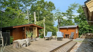 Una terraza de madera con dos sillones, una mesita y una cabaña de madera en un área boscosa.