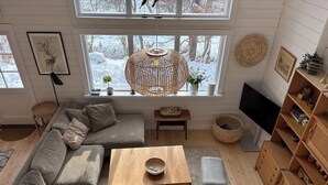 Una sala de estar moderna con un sofá, sillas, una mesa de centro de madera, televisión y un ventanal con vistas a un paisaje nevado.