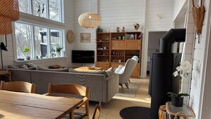 Una sala de estar con sofá, mesa de comedor, sillas, televisor, estantería y chimenea.