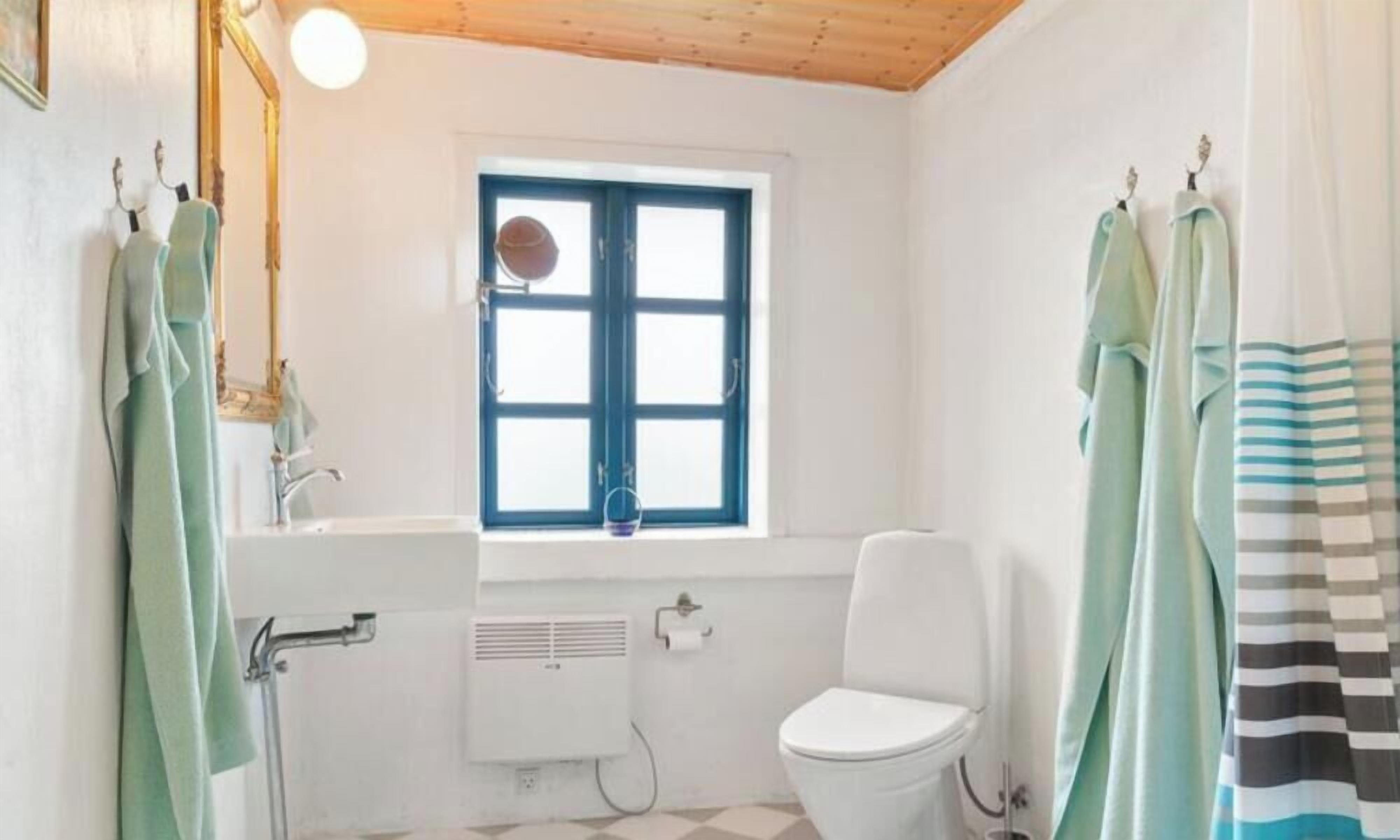 A bathroom with a white toilet, a window with blue shutters, and towels hanging on hooks.
