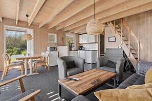 Ein modernes Interieur mit Holzbalkendecke, einer Essecke mit rundem Tisch und Stühlen, einer Couch und einer Küche im Hintergrund.
