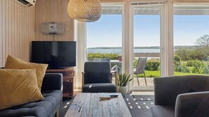 Ett vardagsrum med en tv, en soffa och ett soffbord, en krukväxt och utsikt över omgivningarna.