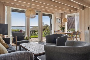 A modern living room with a wooden ceiling, large windows, and a view of the outdoors. - Holiday home with lovely view of Lillebælt (Fredericia)