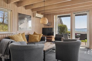 A modern living room with a sofa, chairs, a TV, and a large window with a view. - Holiday home with lovely view of Lillebælt (Fredericia)