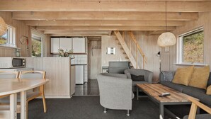 Ett kompakt bostadsutrymme med kök, matplats och sittgrupp, med träpanel på väggarna och en trappa.