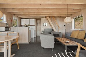 Un espace de vie compact comprenant une cuisine, un coin repas et un coin salon, avec des murs en bois et un escalier.
