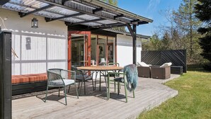 Un terrazzo in legno con mobili da esterno, una pergola e una porta vetrata che dà su un'area coperta.