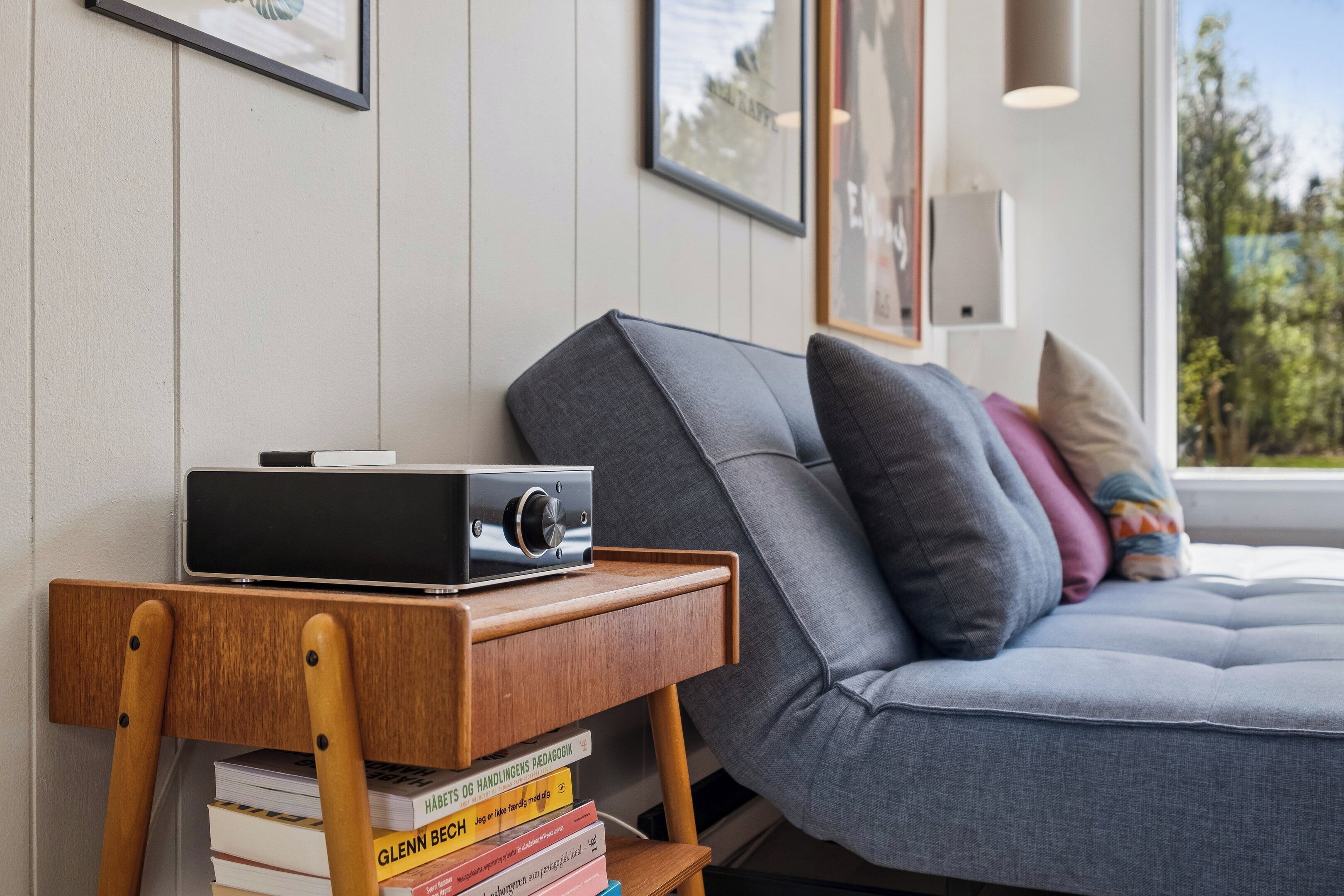 A modern living room with a grey sofa, a small wooden side table with books, and a framed picture on the wall.