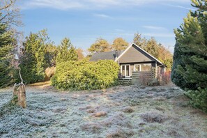Een huis met een schuin dak, omringd door weelderige begroeiing en een bevroren grond.