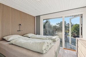 A bedroom with a bed, a bedside table, a lamp, and a sliding glass door leading to an outdoor deck. - Quiet holiday in Hemmet 300 m to water (Hemmet)