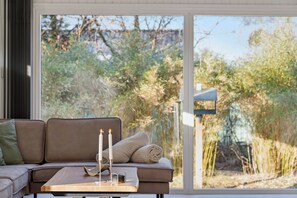 A modern interior with a sofa, a table with candles, and a view of greenery outside. - Quiet holiday in Hemmet 300 m to water (Hemmet)