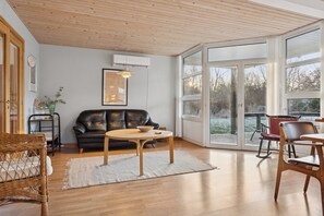 A spacious living area with a black leather sofa, a round wooden coffee table, and a glass door leading to an outdoor deck. - Cozy wooden cottage close to nature and beach (Vig)